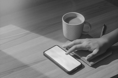 person placing phone face down beside a notebook and coffee
